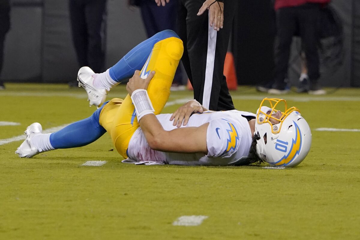 Los Angeles Chargers quarterback Justin Herbert holds his leg after being hit.