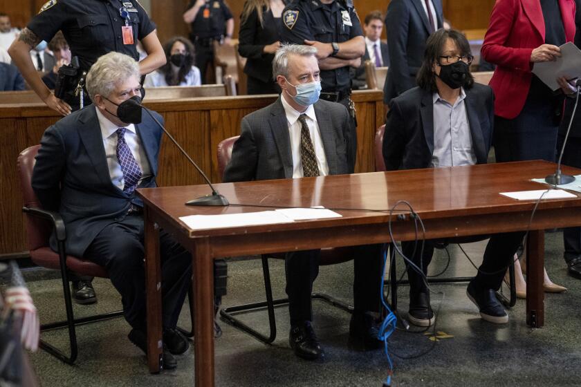 Three men in masks sit at a defendants table in a courtroom