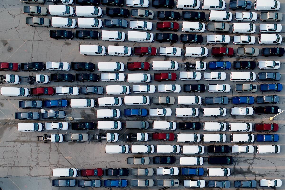 In this aerial photo, mid-sized pickup trucks and full-size vans are seen in a parking lot outside a General Motors assembly plant where they are produced Wednesday, March 24, 2021, in Wentzville, Mo. As the U.S. economy awakens from its pandemic-induced slumber, a vital cog is in short supply: the computer chips that power our cars and other vehicles, and a vast number of other items we take for granted. Ford, GM and Stellantis have started building vehicles without some computers, putting them in storage with plans to retrofit them later. (AP Photo/Jeff Roberson)