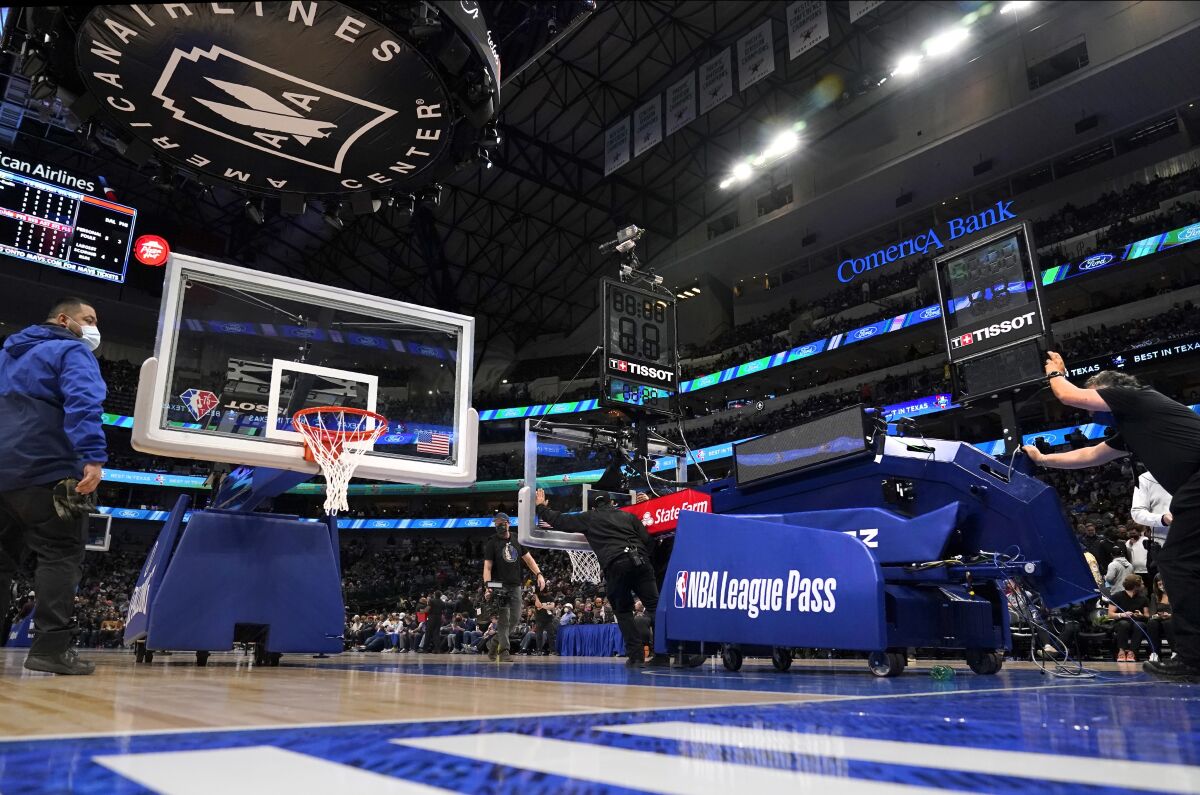Employees at American Airlines Center prepare to install a new rim, board and stanchion, left, after a mechanical difficulty with the one that had been used, right, during the first half of an NBA basketball game between the Philadelphia 76ers and the Dallas Mavericks in Dallas, Friday, Feb. 4, 2022. (AP Photo/Tony Gutierrez)