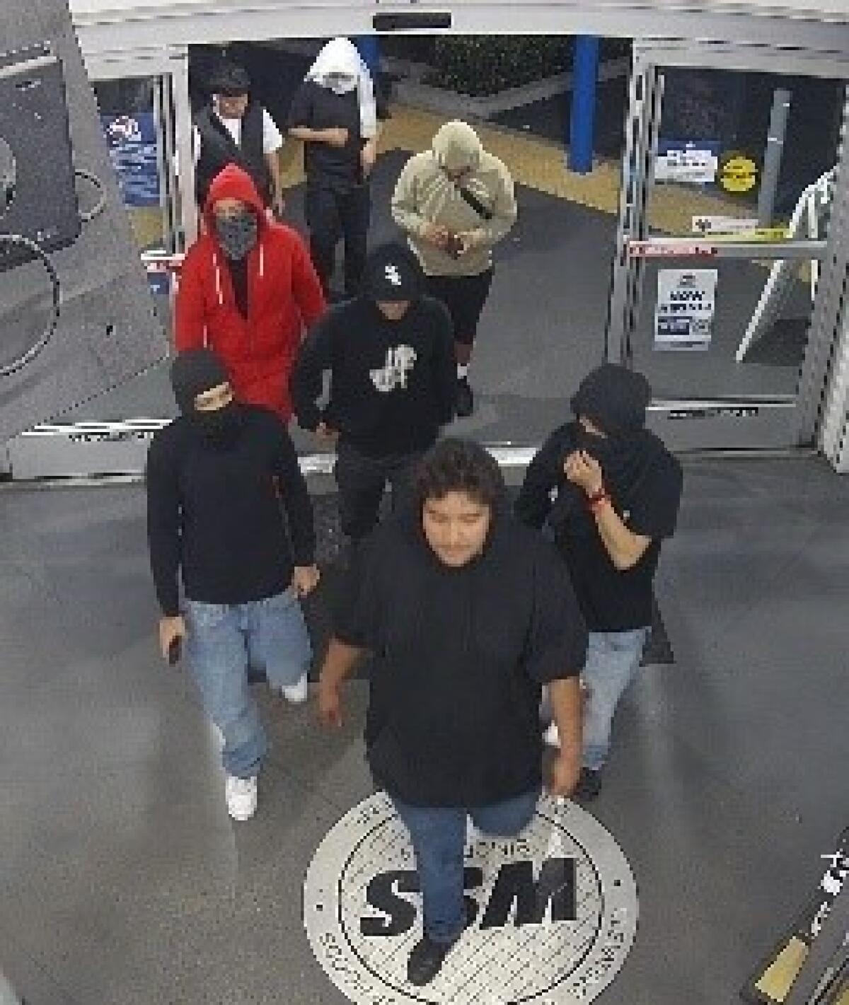 A group of young people, some with faces hidden, walk into a store in a frame from overhead security camera