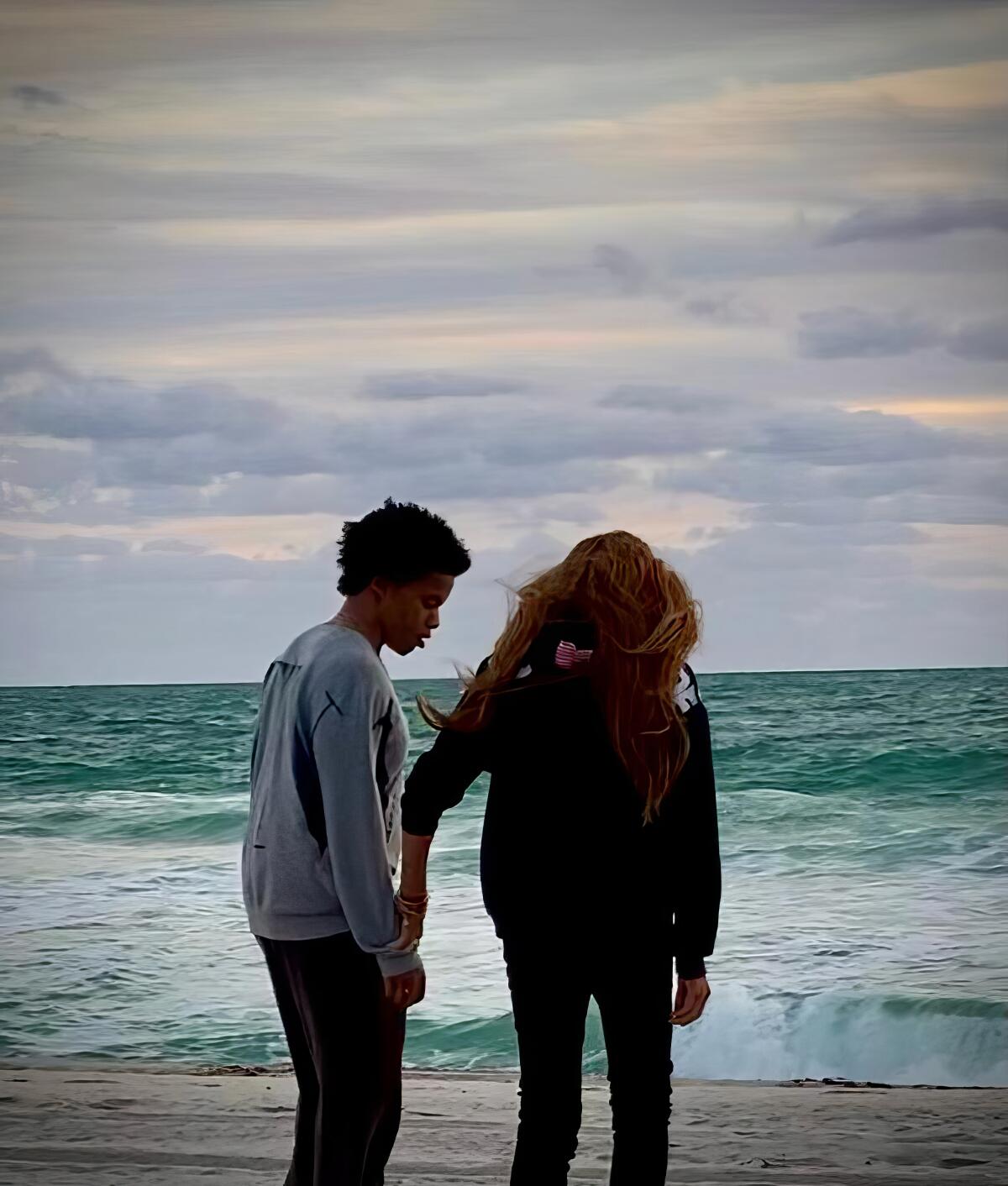 Two people walking on the beach looking at ocean waves.