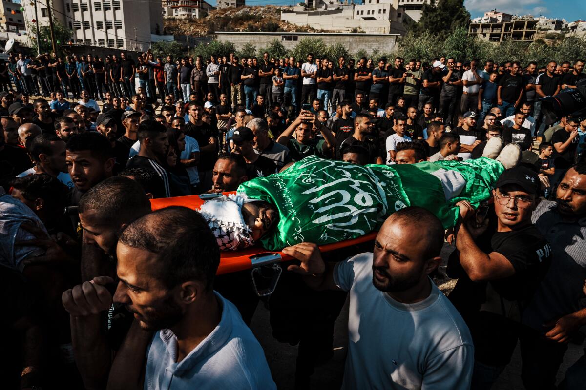 A body wrapped in a Palestinian flag is carried on the shoulder of men in a large crowd of mourners