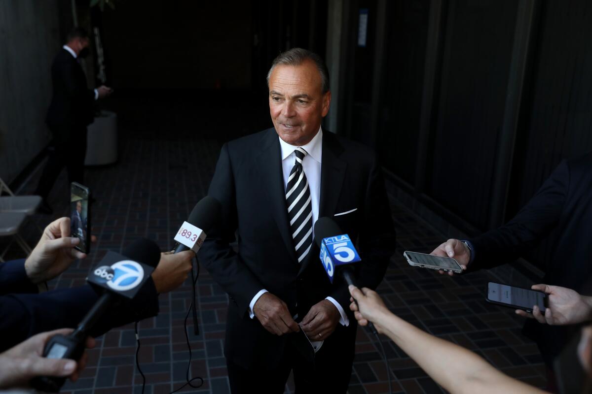 Rick Caruso speaks to reporters holding microphones and phones toward him. 
