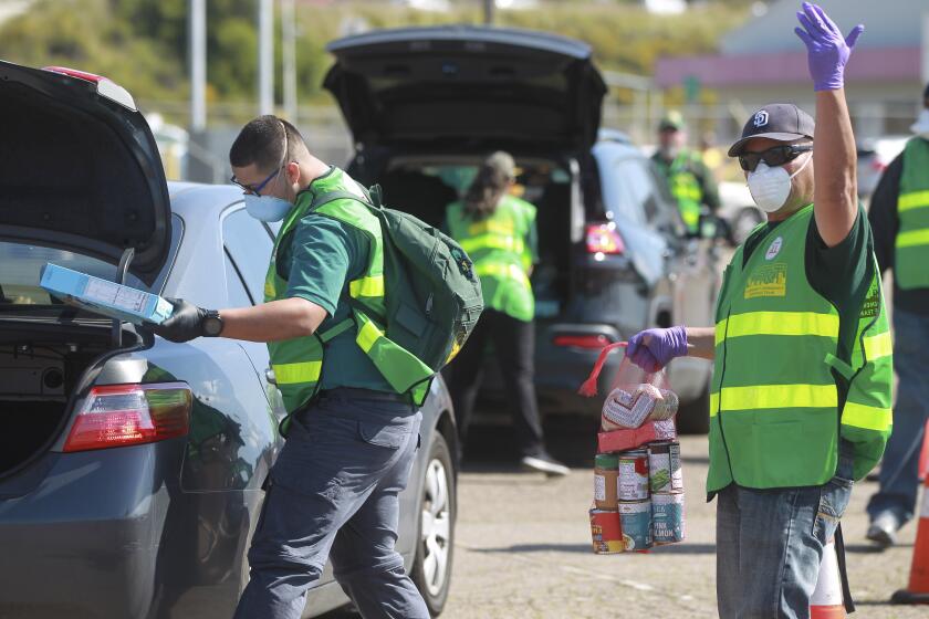 Carlos Moran, a volunteer from the Community Emergency Response Team, signals the next car in line to pull forward as fellow CERT volunteer Christian Rodriguez places a box of cereal into the trunk of a car during the Mass Emergency Food Distribution, put on by the San Diego and Imperial counties Labor Counsel and the San Diego Food Bank, at SDCCU Stadium on Saturday March 28, 2020 in San Diego, California.