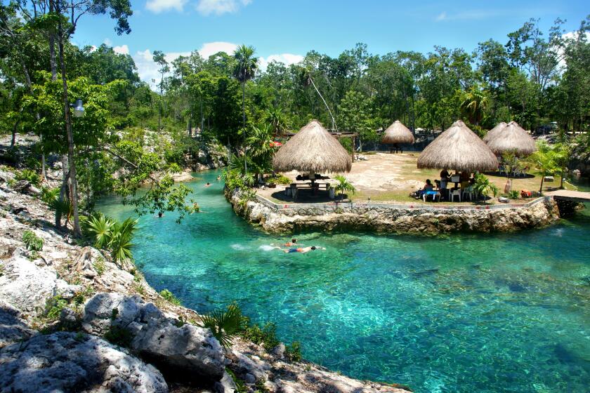 A cenote offers crystal-clear swimming, with picnic areas for tourists and local families in Tulum.