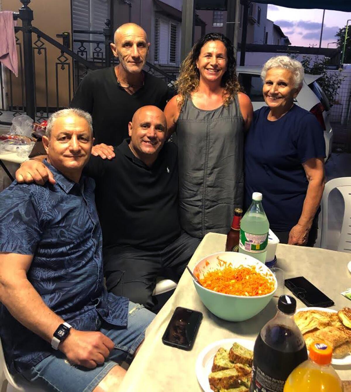 Five people posing by table of food, two of them seated, most with arms around one another