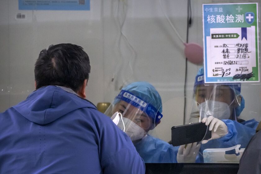 A worker wearing a protective suit administers a COVID-19 test at a coronavirus testing site in Beijing, Wednesday, Oct. 5, 2022. (AP Photo/Mark Schiefelbein)