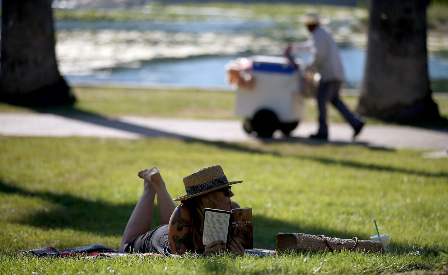 Next to Echo Park Lake, Mishelle Parry reads in the shade as an ice cream vendor walks by.