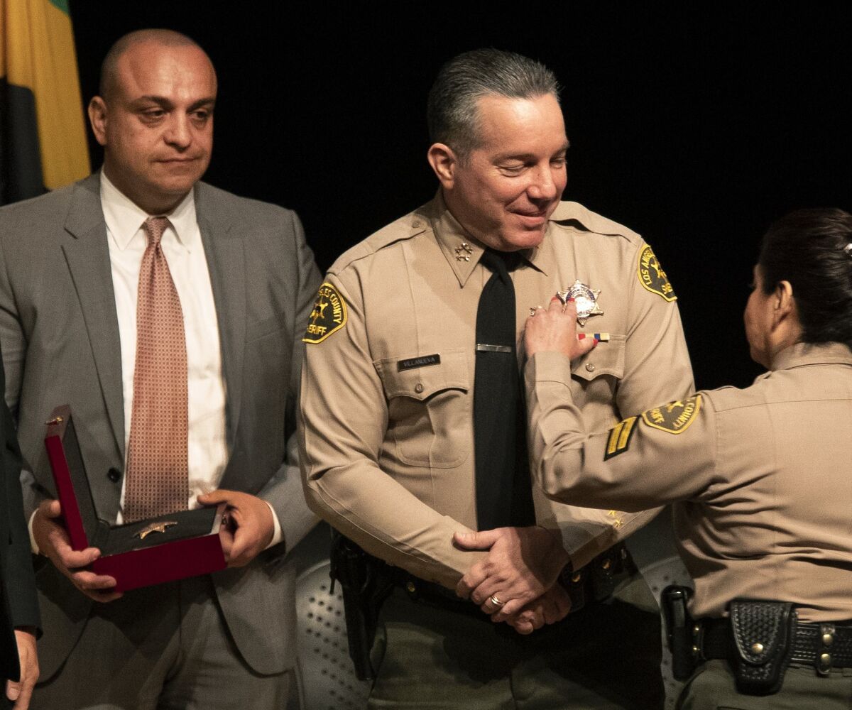 A badge is pinned onto Sheriff Villanueva. Carl Mandoyan looks on