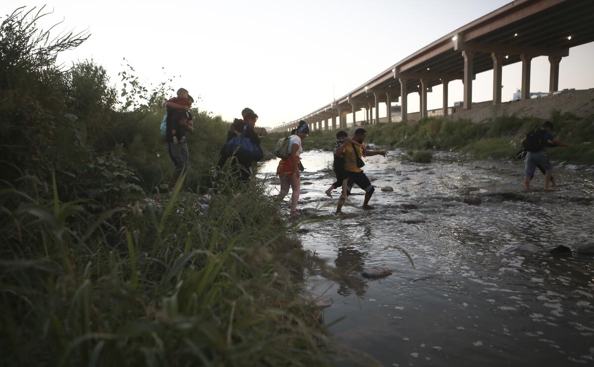 Venezuelan migrants walk across a shallow river 
