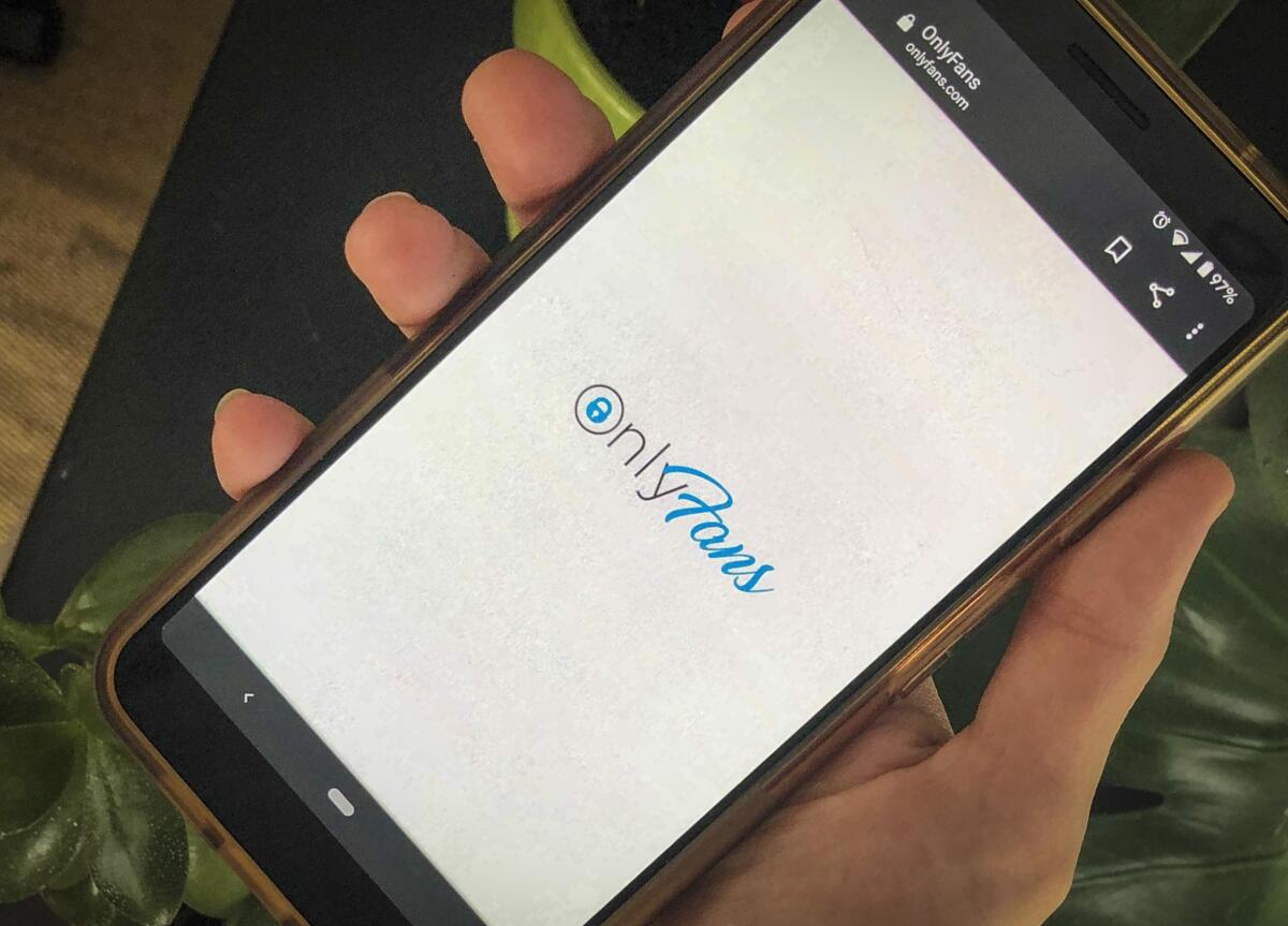 A hand holding a smartphone showing the OnlyFans site