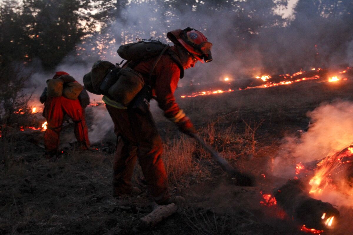 A firefighter used a shovel as lines of fire burn in a wooded area.