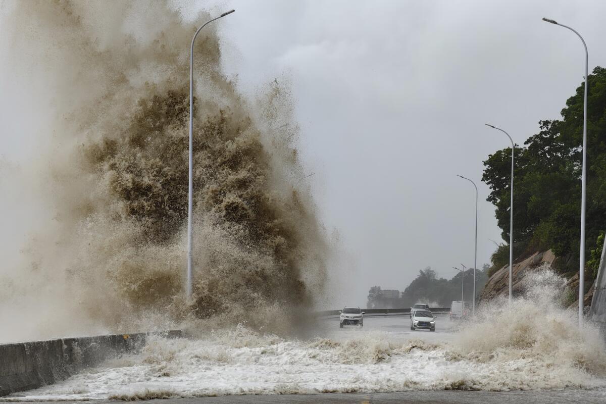 Huge waves lash a road as two cars drive by