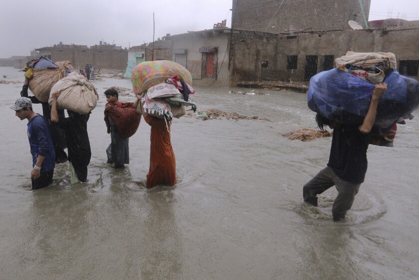 Local residents carry salvaged belongings as they wade through a flooded area during a heavy monsoon rain in Yar Mohammad village near Karachi, Pakistan, Thursday, Aug. 27, 2020. Pakistan's military said it will deploy rescue helicopters to Karachi to transport some 200 families to safety after canal waters flooded the city amid monsoon rains. (AP Photo/Fareed Khan)