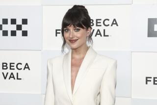 A woman with brown hair and bangs wears a white suit. She poses for pictures at a red carpet event. 