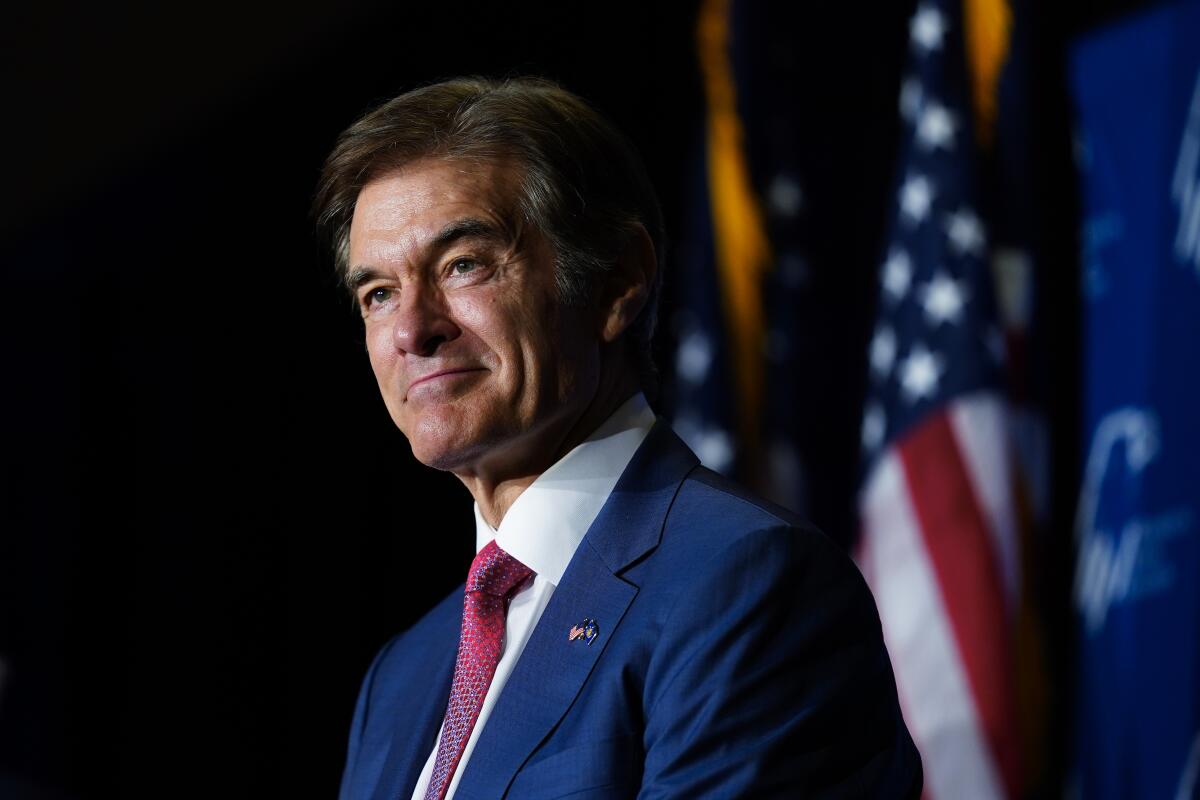 Dr. Mehmet Oz, wearing a blue suit and red tie, smiles on stage.