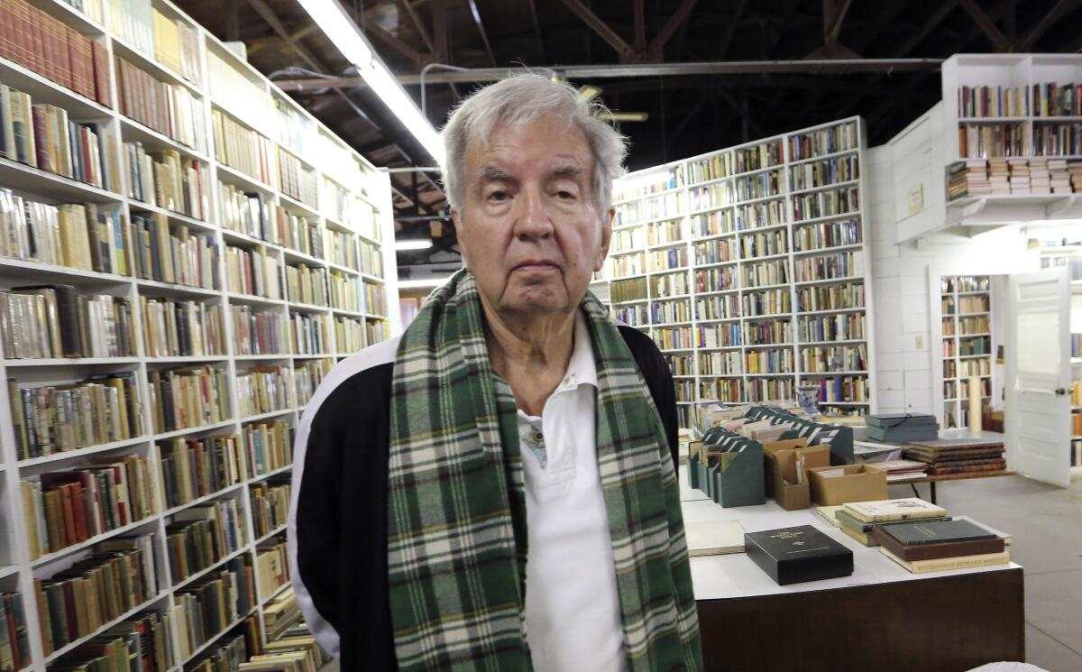 Larry McMurtry stands in front of shelves stacked with books,