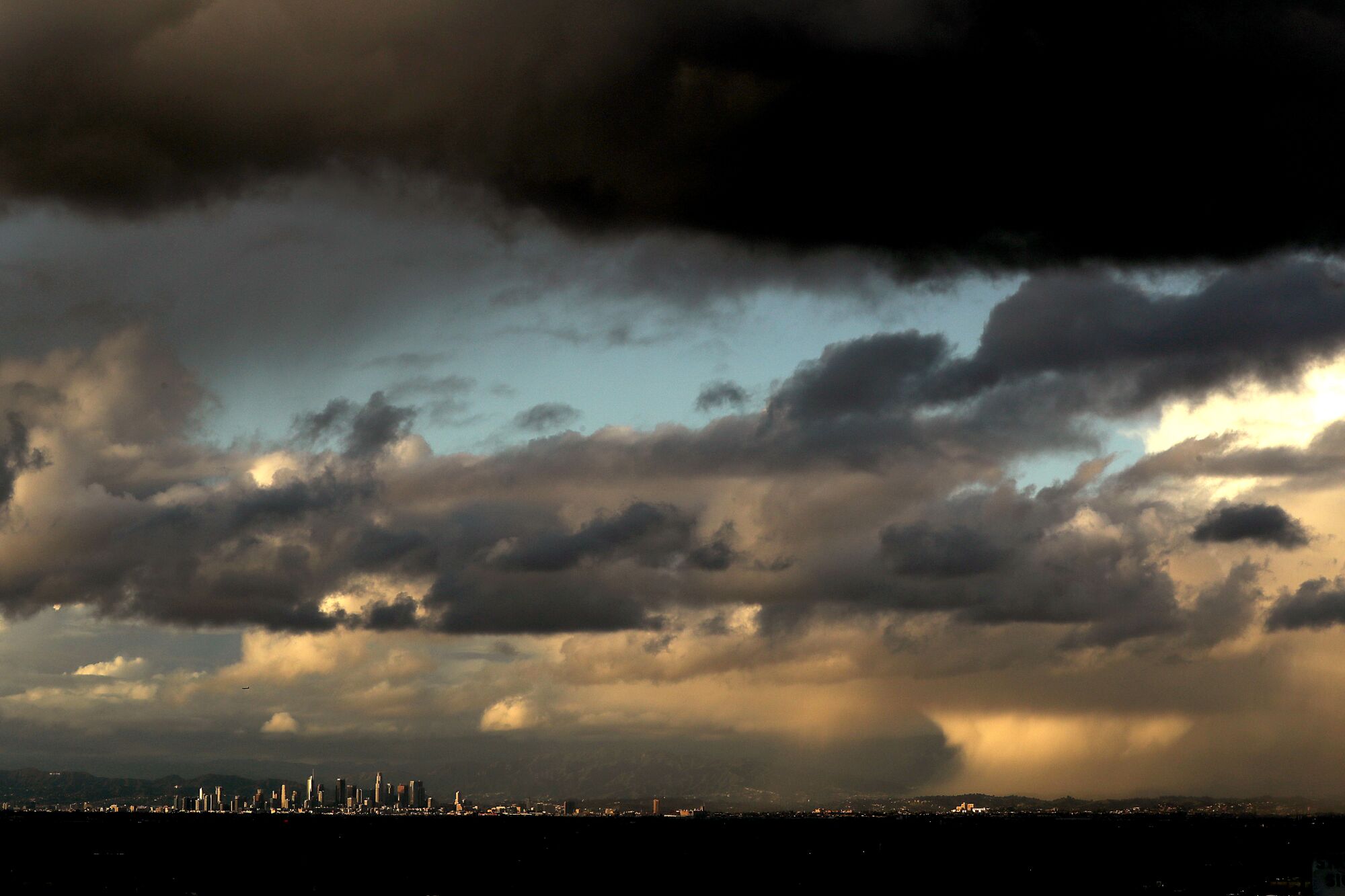 Dark and sunset-lit clouds cover the sky in alternating rows, with the Los Angeles skyline visible at the bottom in distance.