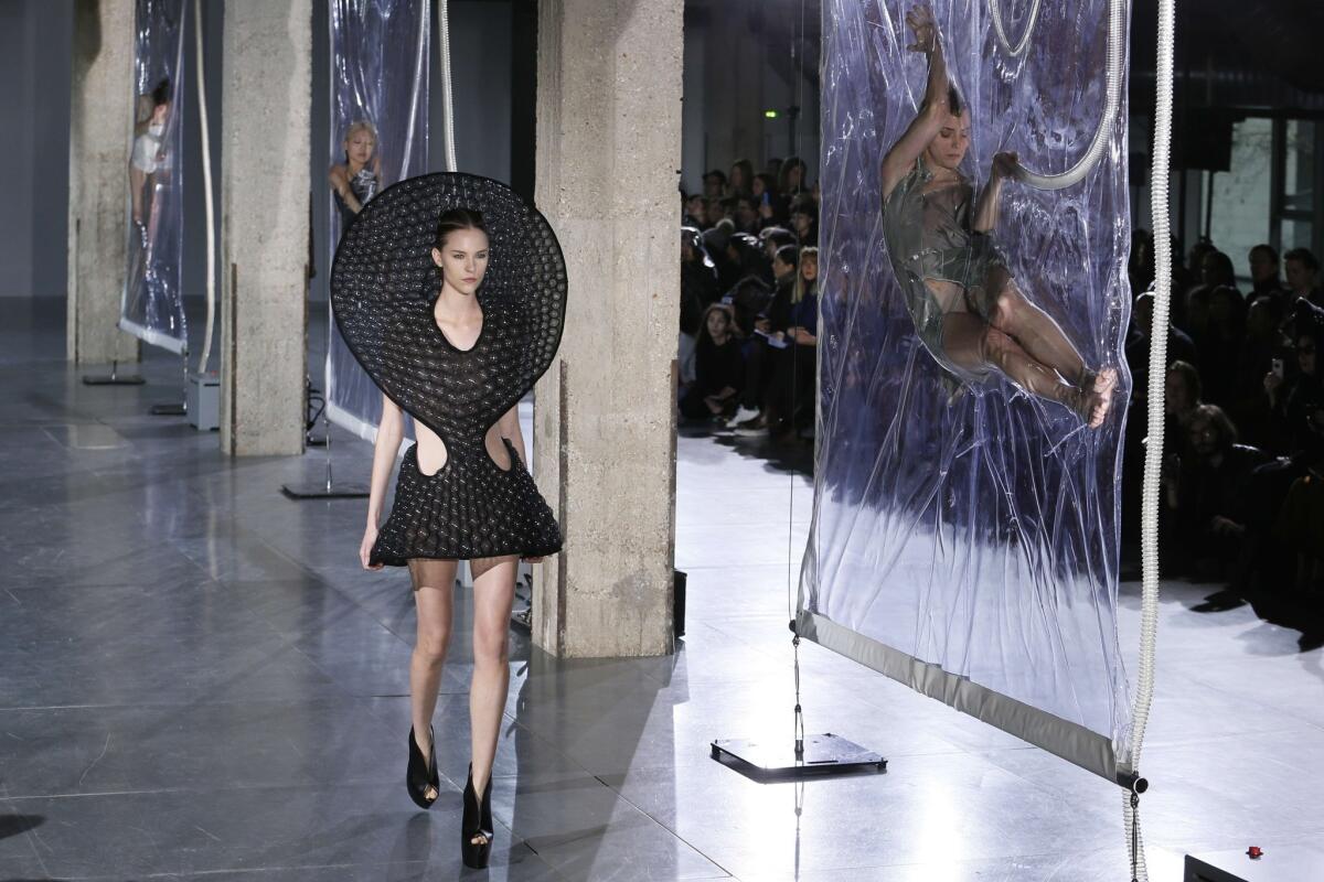 As a model walks on Iris van Herpen's runway, other models hang, shrink-wrapped, in plastic bags.