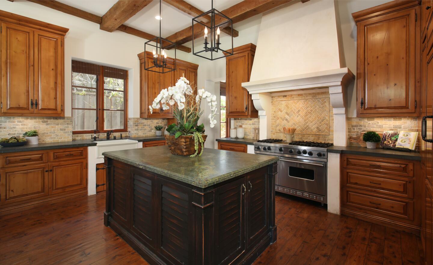 A large island, tile backsplash, wood cabinets and wood floor in the kitchen.