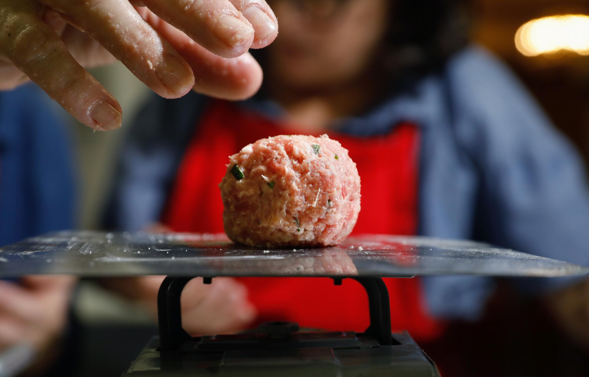 A meatball sits on a small scale with a hand hovering above. 