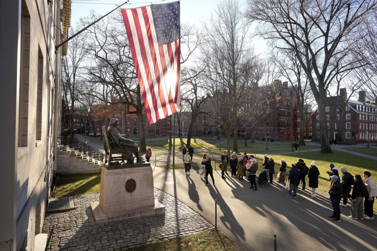 People standing in front of the John Harvard statue on Harvard University's campus in Cambridge, Mass.