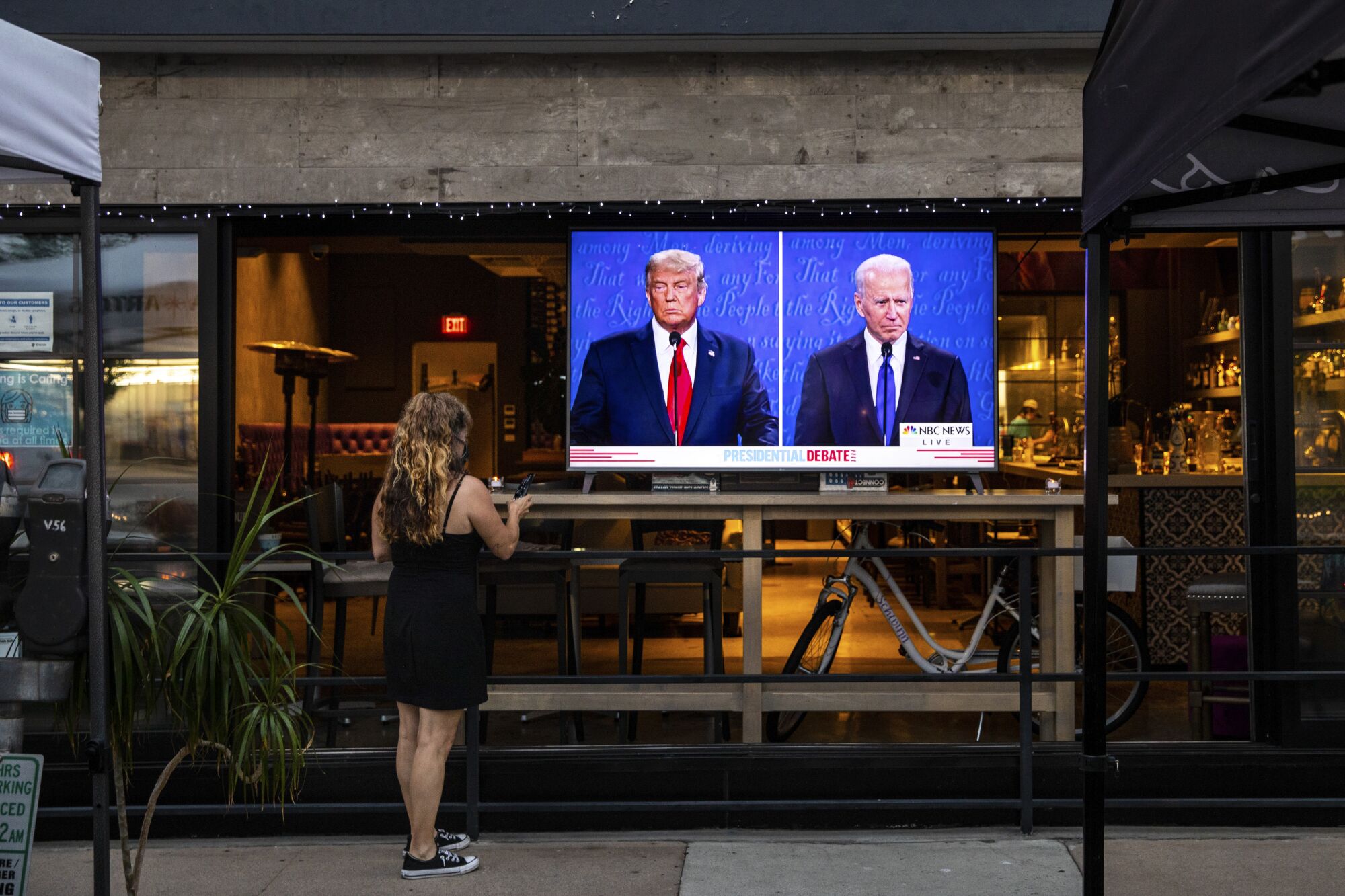 A waitress with a remote standing in front of a TV showing the debate set up in the window of a restaurant