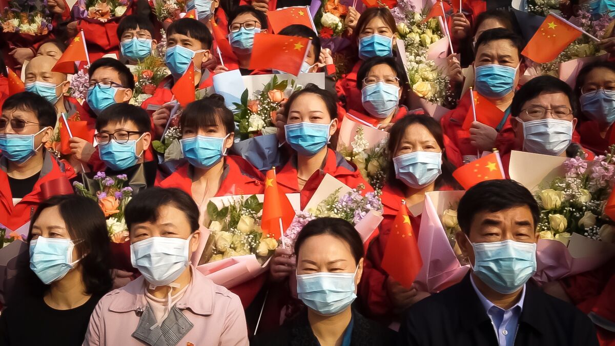 People wearing blue surgical masks hold small Chinese flags