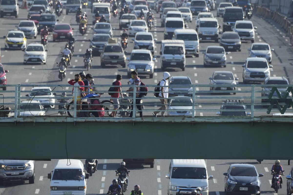 People walk as traffic builds up as the government places the capital on the lowest rung of a five-step pandemic alert system on Tuesday, March 1, 2022, in Quezon city, Philippines. Traffic jams and outdoor crowds were back in the Philippine capital and 38 other cities and provinces Tuesday after officials allowed businesses and public transport, including shopping malls, movie houses and restaurants, to operate at full capacity as COVID-19 cases continued to drop with more vaccinations, officials said. (AP Photo/Aaron Favila)