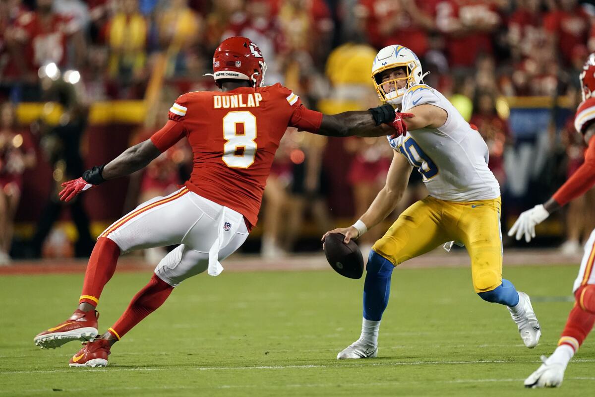 Los Angeles Chargers quarterback Justin Herbert, right, scrambles as Kansas City Chiefs defensive end Carlos Dunlap II (8) defends during the first half of an NFL football game Thursday, Sept. 15, 2022, in Kansas City, Mo. (AP Photo/Charlie Riedel)