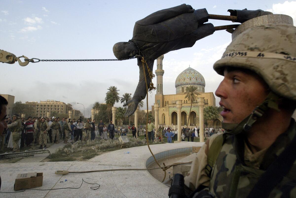 Iraqi civilians and U.S. soldiers pull down a statue of Saddam Hussein in downtown Baghdad on April 9, 2003.