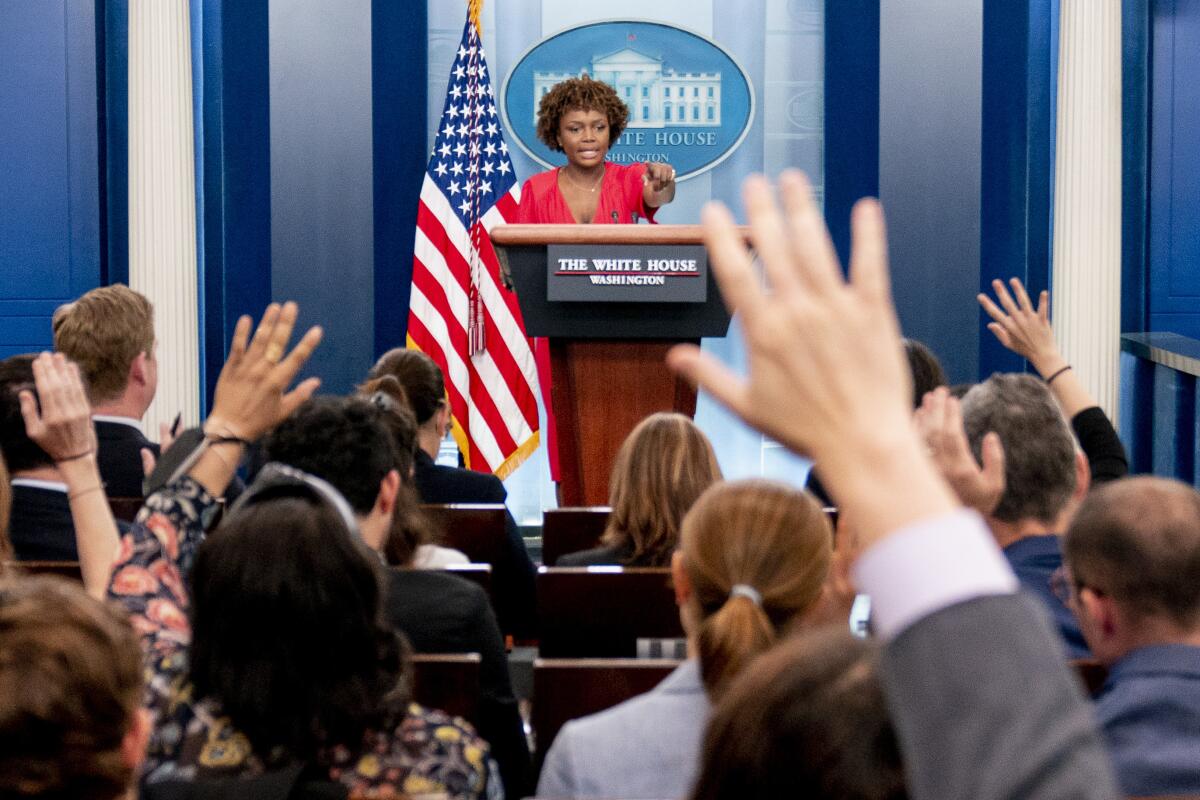 A woman at a podium points as people raise their hands to ask questions.