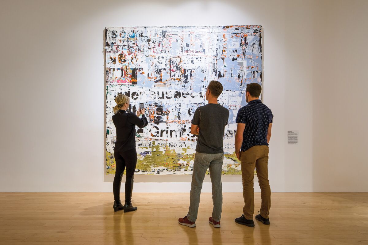 Three people stand looking at a large painting on a wall in a museum.