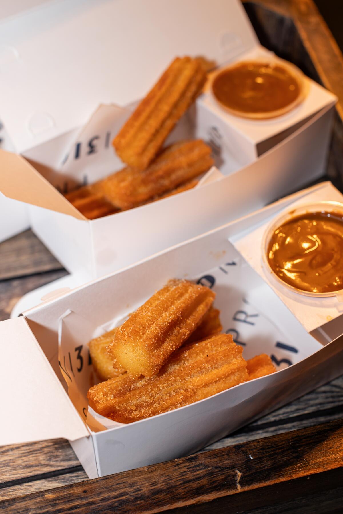 Short churros served with cups of caramel sauce