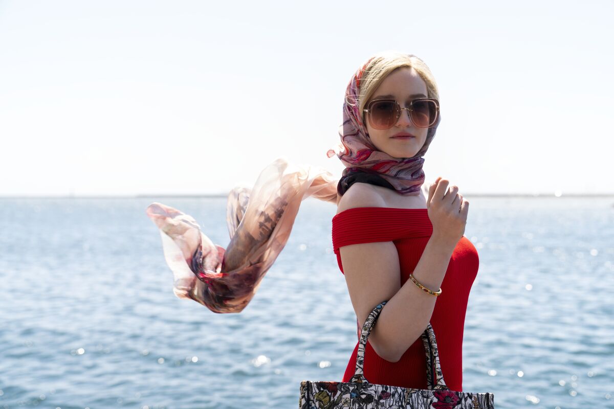 A woman in a red dress and head scarf stands before a glimmering sea.
