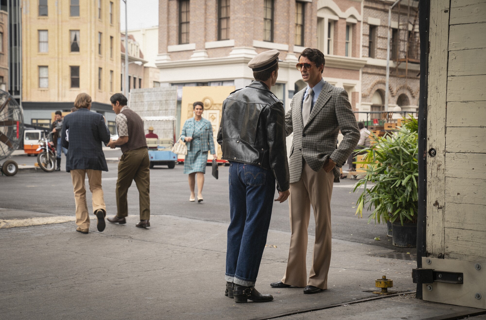 A man in a suit stands in the street talking to a man in a leather jacket and jeans.