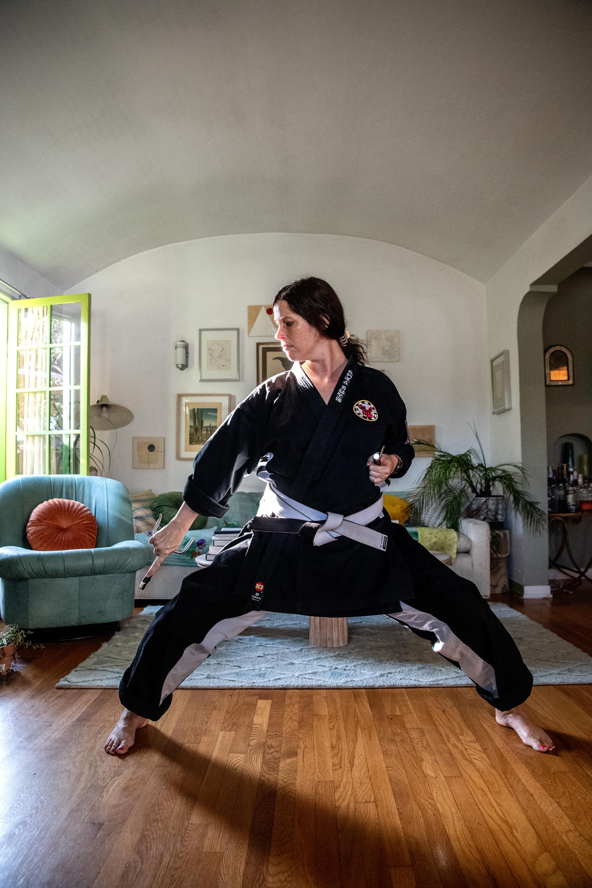 Sally Montana standing in a living room, wearing a gi and striking a martial arts stance.
