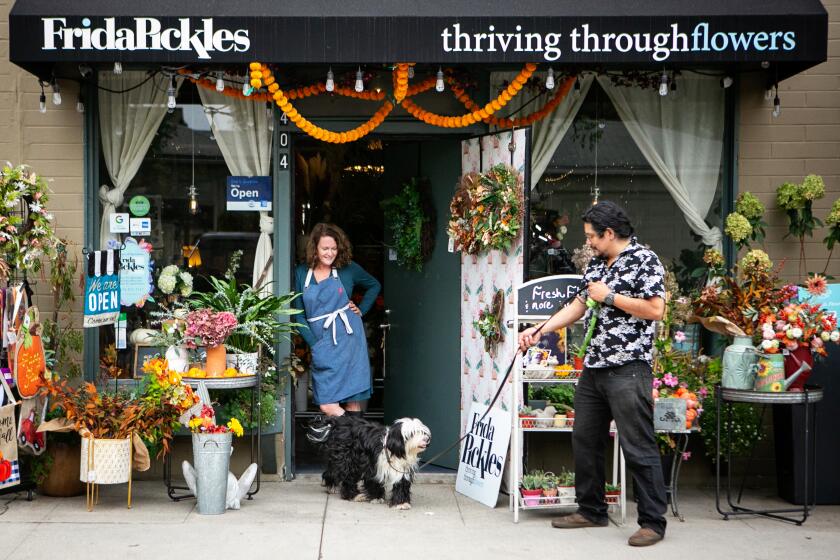 SAN GABRIEL , CA - OCTOBER 07: Owners of Fridas Pickles, a Flower, plant and gift shop, Susan and Juan Sanchez stands in-front of their shop with their dog Fridas Pickles their shops namesake on Thursday, Oct. 7, 2021 in San Gabriel, CA. (Jason Armond / Los Angeles Times)