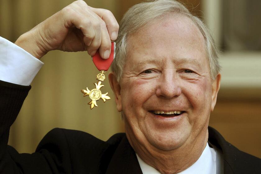 FILE - In this Nov. 28, 2011 file photo, Tim Brooke-Taylor holds his OBE after being presented it by Queen Elizabeth, outside Buckingham Palace in London. British comedian Tim Brooke-Taylor, a member of comedy trio The Goodies, has died after contracting the new coronavirus. He was 79. Brooke-Taylor’s agent says he died Sunday, April 12, 2020 “from COVID-19.”(John Stillwell/PA via AP)