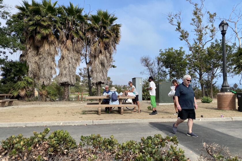 Volunteer Jan Greenberg walks back to the food set up after assisting men at the table at Doheny State Beach on June 16.