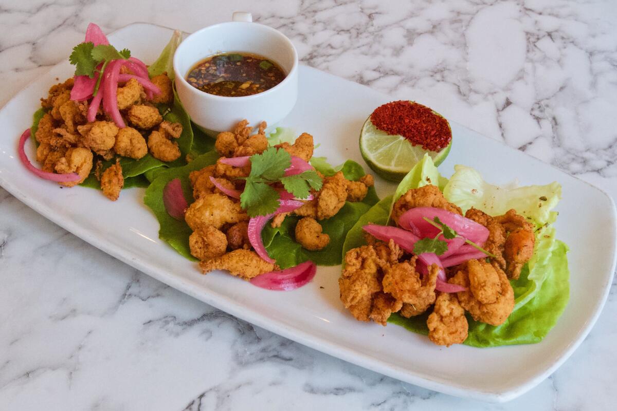 A rectangular white plate of three lettuce cups filled with fried crawfish on a marble tabletop