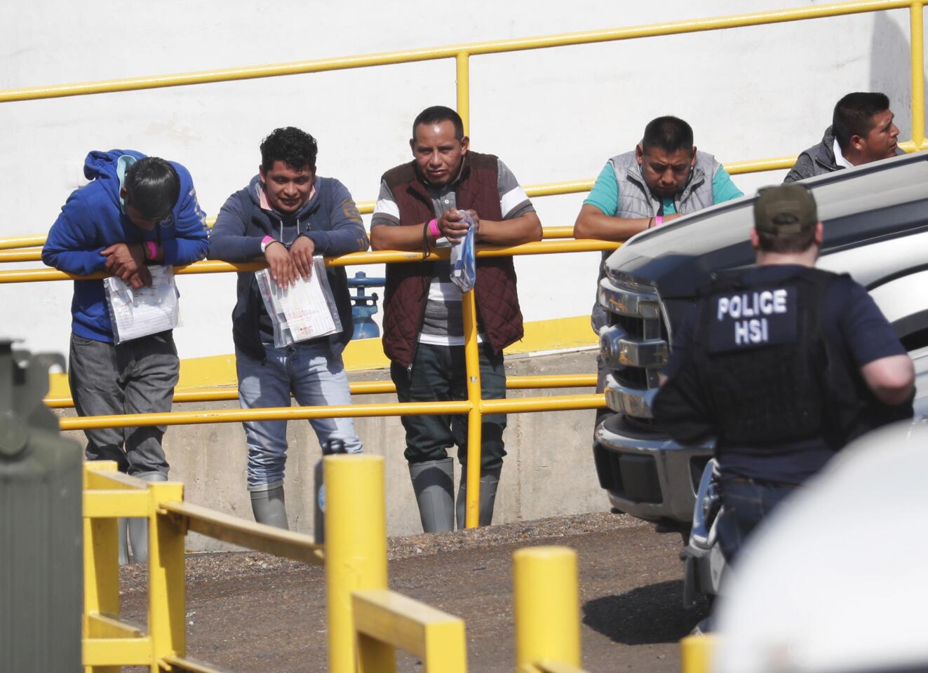 Handcuffed workers await transportation to a processing center following a raid by U.S. immigration officials at a Koch Foods Inc. plant in Morton, Miss.