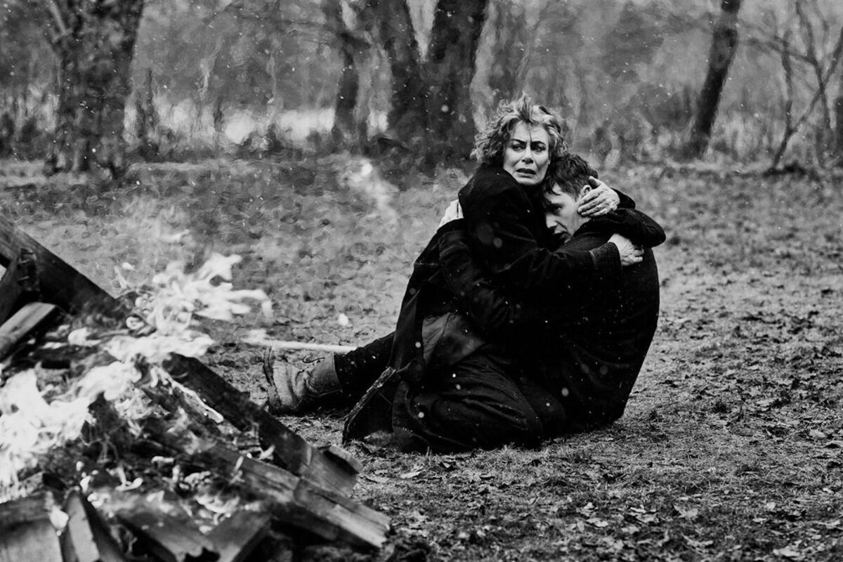 A black-and-white image of a woman cradling a young man beside a fire in the movie "The Righteous."