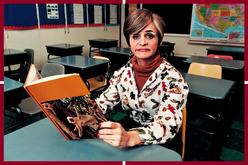 A woman sits at a school desk holding an open book