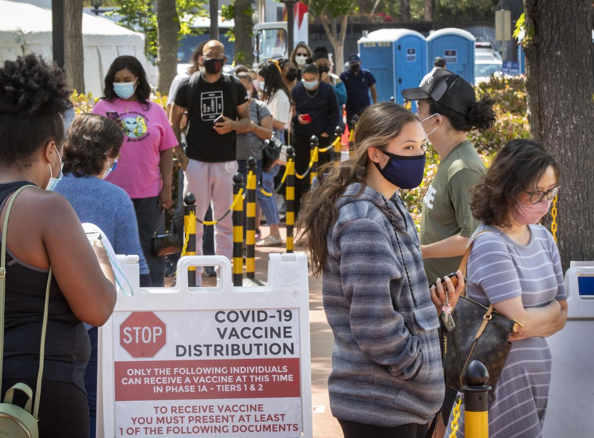 People in masks wait in line at a COVID-19 vaccination site