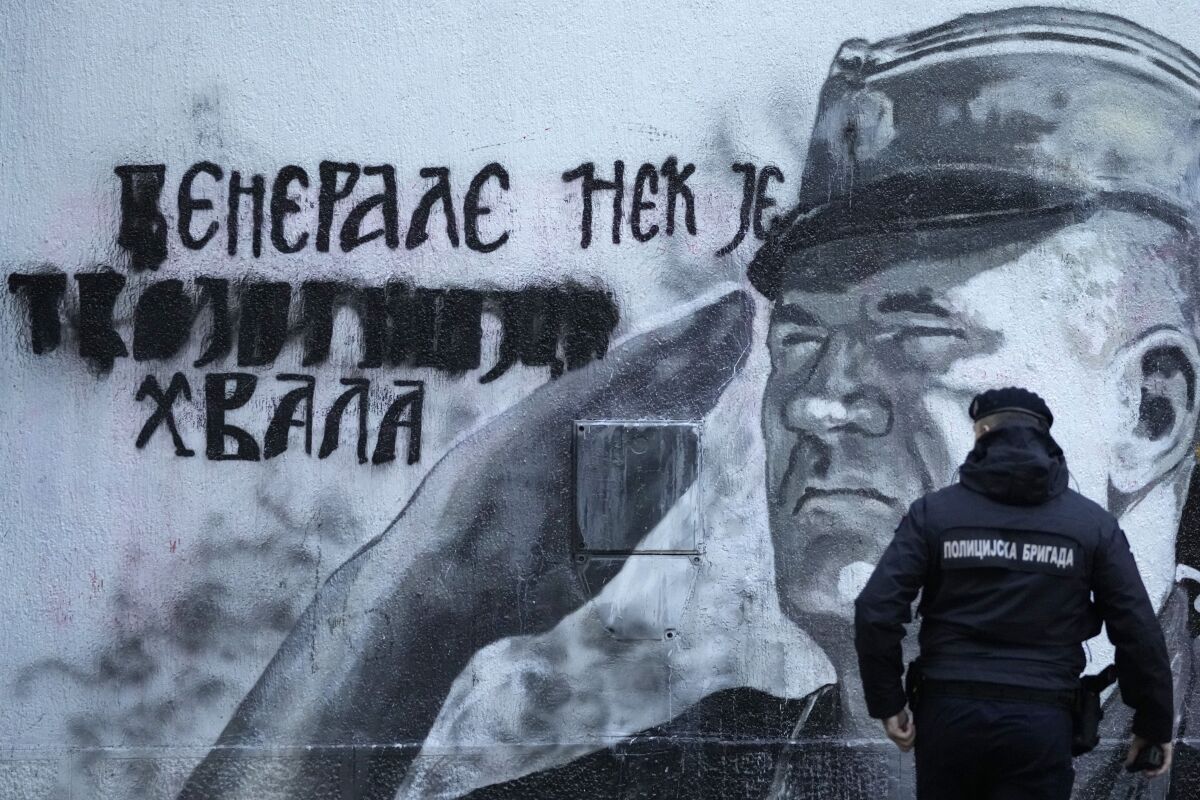 A police officer walks by a mural of former Bosnian Serb military chief Ratko Mladic in Belgrade, Serbia, Tuesday, Nov. 9, 2021. Police officers were deployed Tuesday at the site of a large wall painting in Belgrade of convicted Bosnian Serb wartime commander Ratko Mladic which rights activists wanted to remove. The gathering, which was to coincide with the international day of anti-Fascism and anti-Semitism, was banned by the police which said that they were preventing possible clashes between the activists and the right-wing nationalists who consider the Serb general a hero. (AP Photo/Darko Vojinovic)
