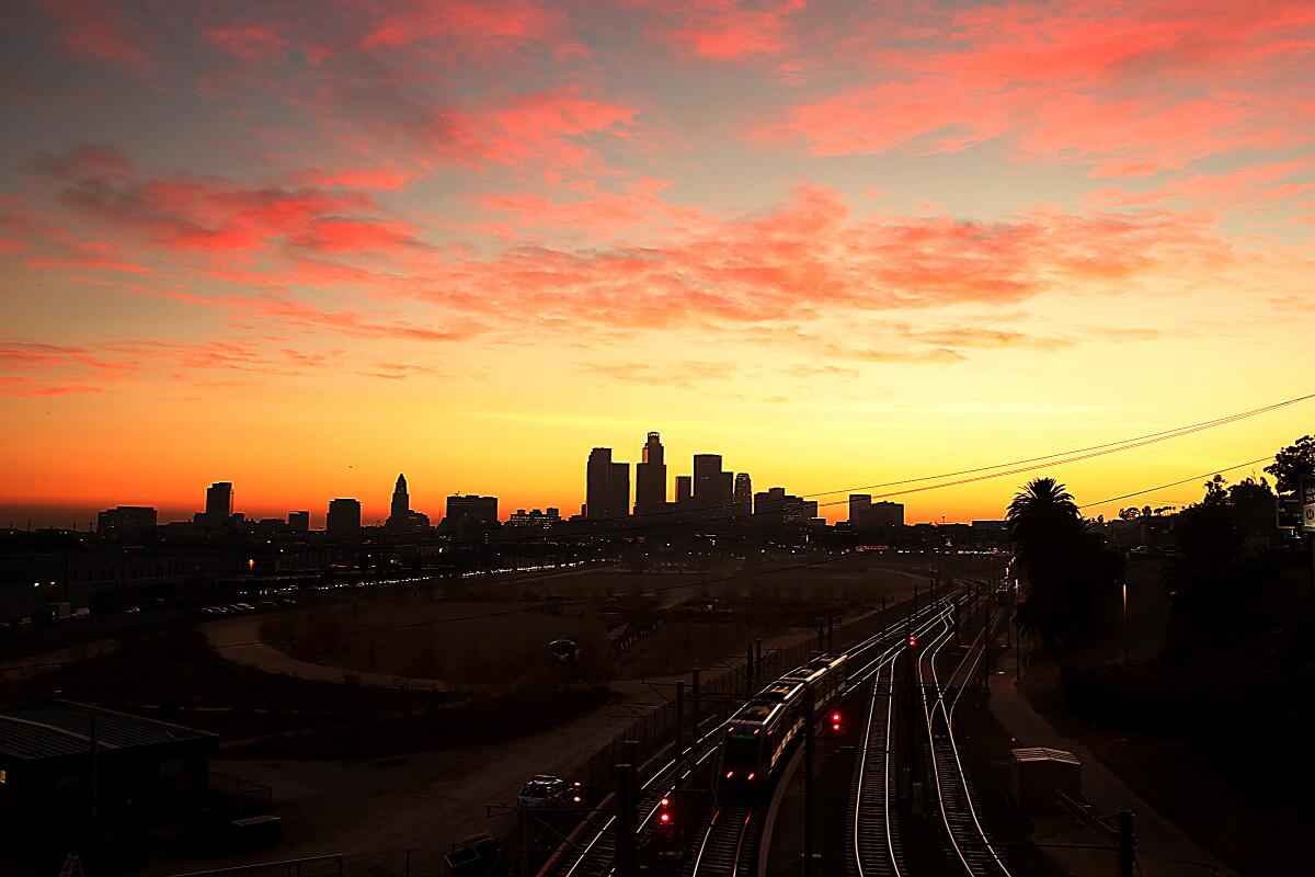 Railroad tracks glisten in the setting sun with the L.A. skyline in the background