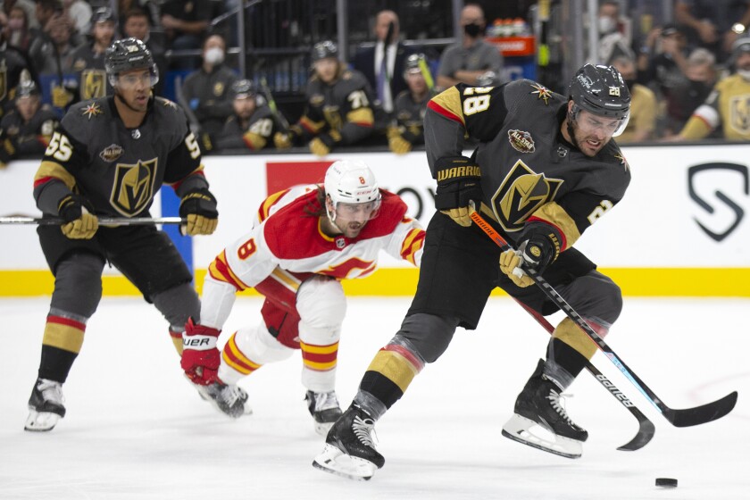 Vegas Golden Knights left wing William Carrier (28) skates with the puck while followed by Calgary Flames defenseman Christopher Tanev (8) and Golden Knights right wing Keegan Kolesar (55) during the second period of an NHL hockey game Sunday, Dec. 5, 2021, in Las Vegas. (AP Photo/Ellen Schmidt)