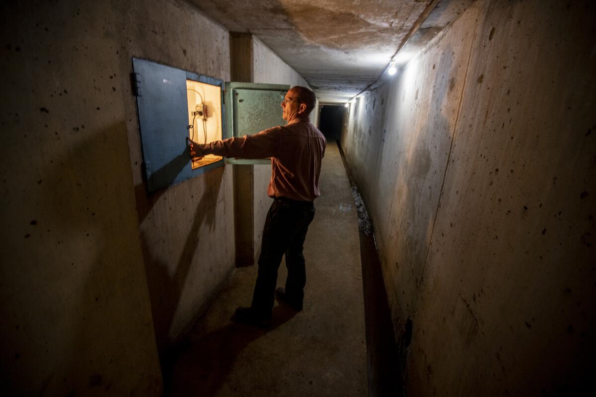 A man looks behind a panel in an empty, unadorned corridor.